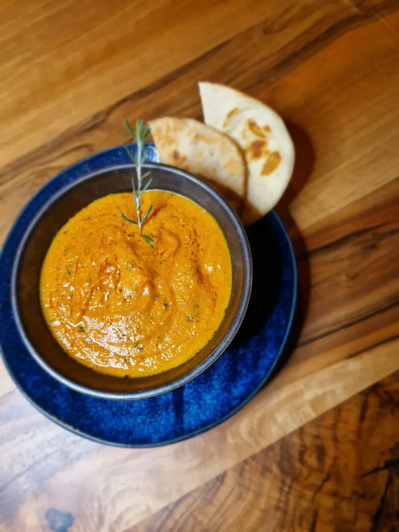 Curry in blauer Schale mit frischem Naan auf dem Holztisch