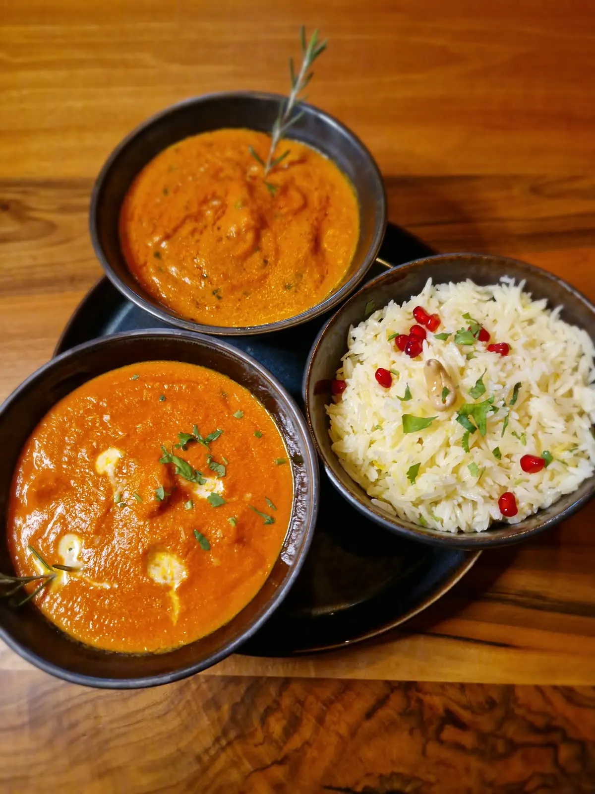 Zwei Curries und Basmati-Reis in dunklen Schalen auf Holz